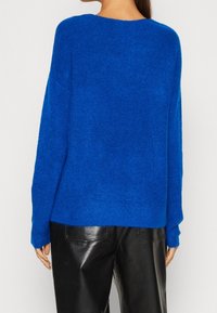 Blå stickad tröja med avslappnad passform, rund halsringning och ribbad struktur. Kombinerad med svarta läderbyxor.