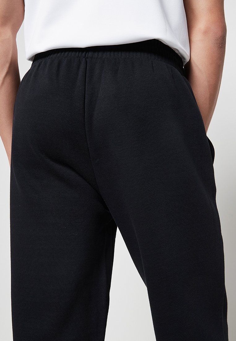 Czarne bawełniane dresy z elastycznym paskiem w talii, o gładkiej fakturze i luźnym kroju, widziane z tyłu.