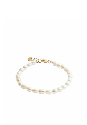 Bracelet avec des perles ovales blanches, un fermoir en or et une petite étiquette en or sur fond blanc.