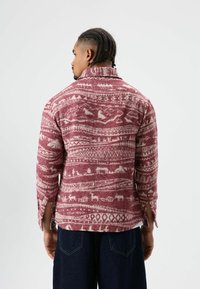 Bordeauxrode en crèmekleurige blouse met patroon en kraag, voorzien van een gestructureerde stof, lange mouwen en zijsplitten aan de zoom.