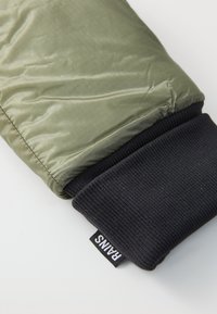 Green quilted jacket sleeve with black ribbed cuff and "RAINS" brand tag on a white background.