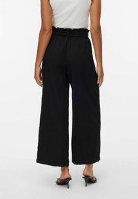 Zwarte wijde broek met een hoogtaille ontwerp, gestructureerde stof en een verstelbare tailleband, gecombineerd met zwarte hoge hakken.