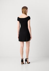 Robe noire à épaules dénudées avec un corsage ajusté et une jupe évasée. Portez-la avec des chaussures à talons aiguilles noires et des brides à la cheville. Texture lisse.