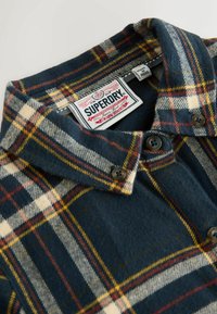 Marinblått flanellskjorta med ett rutmönster i kräm, röd och gul. Har en krage, knäppning och en märkt etikett inuti.