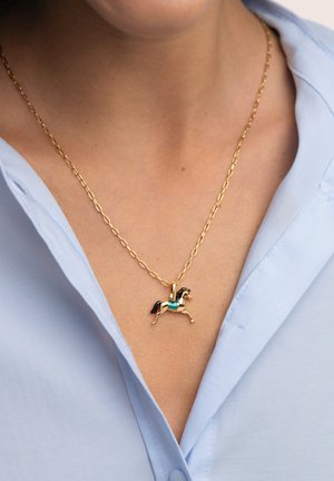 Collier pendentif cheval en or avec des détails turquoise sur une chaîne en or, porté sur une chemise bleu clair à col.