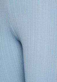 Leggings bleu clair côtelés fabriqués en tissu texturé, avec une coupe ajustée et de subtiles rayures verticales pour plus de détails.