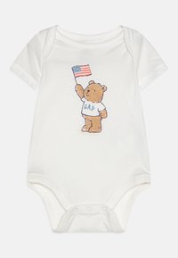 Λευκό βαμβακερό φορμάκι με καρτούν αρκούδα που κρατάει την αμερικανική σημαία, με το "GAP" τυπωμένο στη μπλούζα της σε μπλε χρώμα. Μαλακή υφή και κοντά μανίκια.