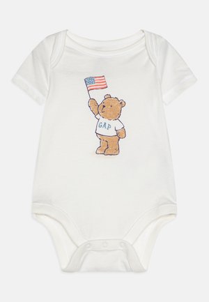 Weißer Baumwollstrampler mit einem Cartoon-Bären, der eine amerikanische Flagge hält, und "GAP" in blauer Schrift auf seinem T-Shirt. Weicher Stoff und kurze Ärmel.