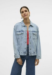 Svetlo modra denim jakna s klasičnim krojem, ki ima prsne žepe, srebrne gumbe in rahlo bledenje. Ustvarjena nad roza majico.