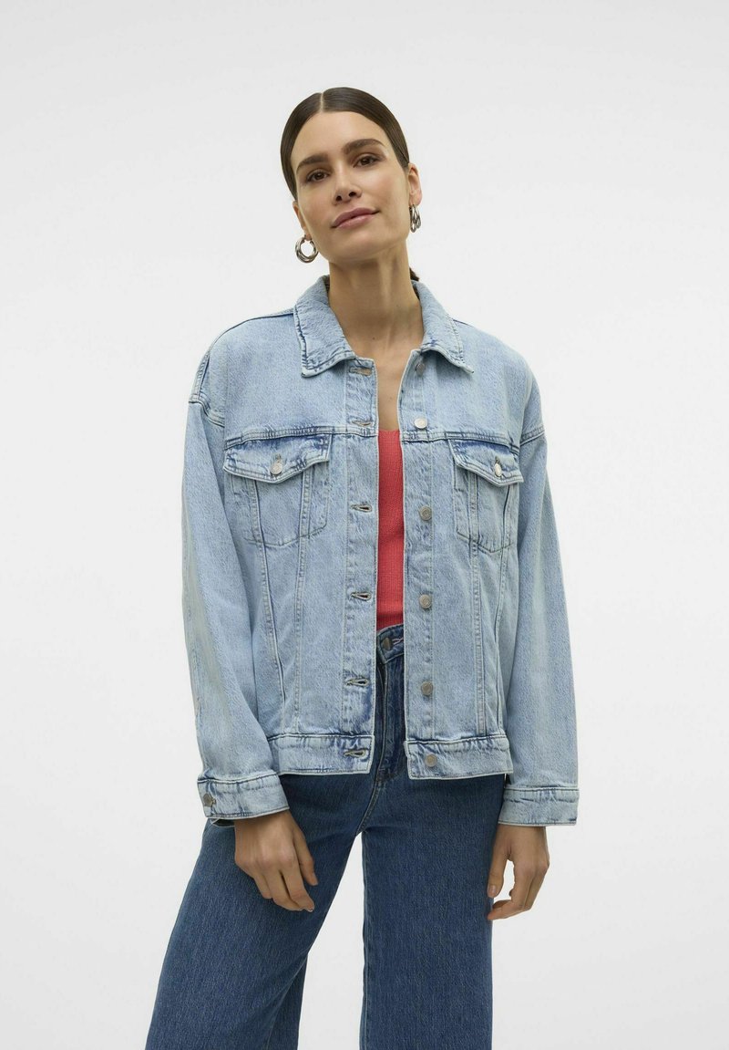 Svetlo modra denim jakna s klasičnim krojem, ki ima prsne žepe, srebrne gumbe in rahlo bledenje. Ustvarjena nad roza majico.