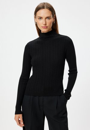 Black ribbed turtleneck sweater with long sleeves, fitted design, and textured fabric. Paired with loose black trousers.