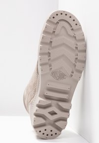 Suela de una bota beige de Palladium con un patrón de agarre texturizado de diseño geométrico y un logotipo de la marca prominente.