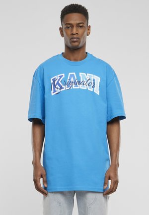 Blå bomulds T-shirt med fed hvid og navy tekst "KANI" og "Kriginator". Korte ærmer, rund hals og afslappet pasform.