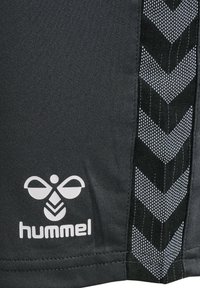 Schwarze sportliche Shorts aus strukturiertem Stoff, mit einem auffälligen weißen Logo und einem markanten Chevron-Muster aus Mesh an der Seite.