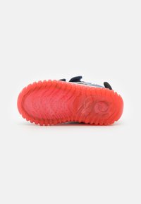 Zapato infantil con suela texturizada de un brillo naranja, parte superior en azul marino y dos correas de Velcro, mostrado desde la parte inferior sobre un fondo blanco.