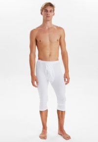 White cotton fitted leggings with a mid-calf length, elastic waistband, and a front pouch detail; smooth texture and lightweight design.
