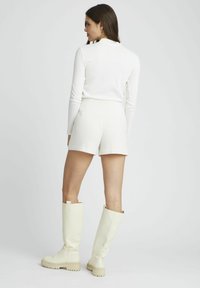 Haut à manches longues blanc côtelé avec col montant, associé à un short blanc texturé et des bottes crème montantes. Design simple et moderne.