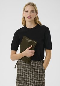 Czarny sweter krótki rękaw, spódnica w kratę oraz błyszcząca oliwkowo-zielona kopertówka. Kopertówka ma elegancki, prostokątny kształt z detalem zamka błyskawicznego.
