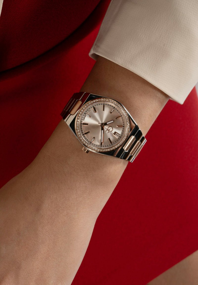 Metallur klocka med armband i roséguld och silverfärg, rund urtavla, strukturerad ljusrosa skiva och boett pryd med små kristaller.