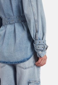 Lichtblauwe denim shirt met een ceintuur in de taille, voorzien van knoopmanchetten en een afgeronde zoom. Gestructureerde stof met een voorzakdetail.