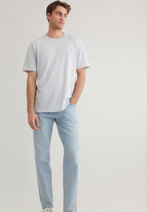 Light blue short-sleeve t-shirt with a round neckline and small logo detail on the left chest, paired with light blue jeans and white sneakers.