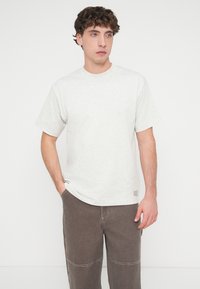 Ανοιχτό γκρι βαμβακερό t-shirt με στρογγυλή λαιμόκοψη και κοντά μανίκια, με μικρό ταμπελάκι του бренδου στο τελείωμα και άνετη εφαρμογή.