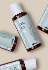 Bruine glazen flessen met een lichtblauwe label, met de tekst "VIND PLEZIER" en "Make-Up Entferner." Witte dop en abstracte ontwerpaccenten.