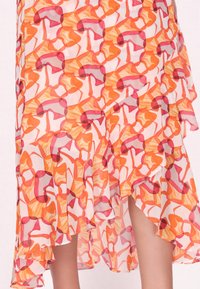 Vloeiende rok van doorschijnende stof met een kleurrijk abstract patroon van rode, oranje en gele vormen; de zoom heeft een golvend ontwerp.
