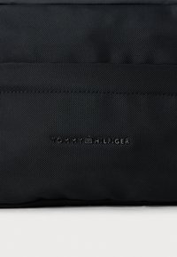 Must-have mustsnahk kott tekstuuriga pinnaga. Ühel küljel on reljeefne "TOMMY HILFIGER" logo, mis tutvustab minimalistlikku disaini.
