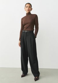 Brown ribbed long-sleeve turtleneck paired with high-waisted, wide-leg black trousers. Black belt with silver buckle and pointed brown shoes.