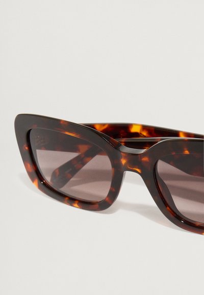 Γυαλιά ηλίου από κερωτό με μεγάλα ορθογώνια πλαίσια και κεκλιμένα καφέ φακούς, με λεία, γυαλιστερή φινίρισμα και κοφτές γωνίες.