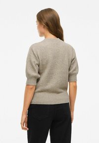 Beige pletený svetr s krátkými nabíranými rukávy, kulatým výstřihem a žebrovaným lemem, nošený s černými džíny. Měkká textura a lehký materiál.