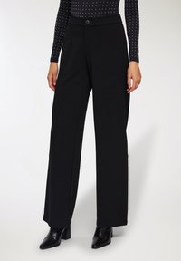 Pantaloni neri a gamba larga realizzati in un tessuto morbido e strutturato, con una cintura liscia, chiusura frontale con bottone e tasche laterali.