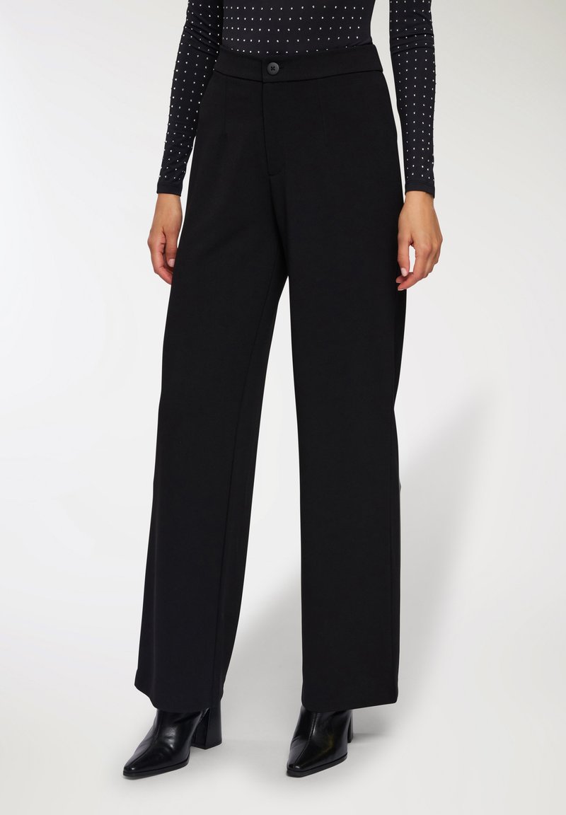 Pantaloni neri a gamba larga realizzati in un tessuto morbido e strutturato, con una cintura liscia, chiusura frontale con bottone e tasche laterali.