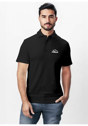 Black polo shirt with a collar, featuring a white mountain logo on the left chest. Short sleeves and smooth fabric. Worn with blue jeans.