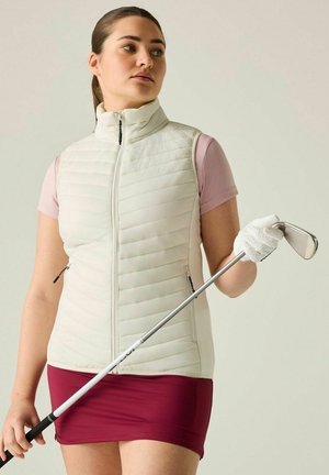 Vrouw die een witte mouwloze vest en een bordeauxrode rok draagt, houdt een golfclub vast met een witte handschoen aan haar rechterhand en kijkt naar links.