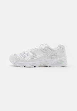 Scarpe sportive bianche realizzate in materiali mesh e sintetici, con punta arrotondata, design con lacci, unità di ammortizzazione visibile e dettagli testurizzati.