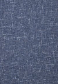 Gros plan sur un tissu bleu tissé avec une texture visible et des accents de fils blancs créant un motif subtil en quadrillage.