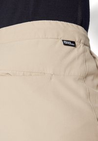 Beige shorts met een gladde textuur, voorzien van een achterzak en een label met het 'Jack Wolfskin' logo nabij de tailleband.