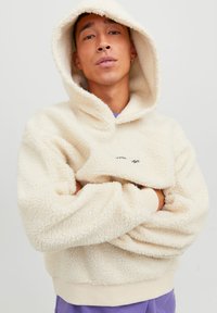 Kremfarget fleece hettegenser med høy krage, synlige sømmer og ribbestrikkede mansjetter. Har en frontlomme og subtilt logo-detalj.