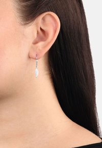 Nära bild av höger öra med mörkt, rakt hår, som bär en liten silverfjäderformad hänge.