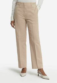 Beiga vida byxor i slät tyg, med en framveck och sidofickor. Bärs med vita klackar med slingback.