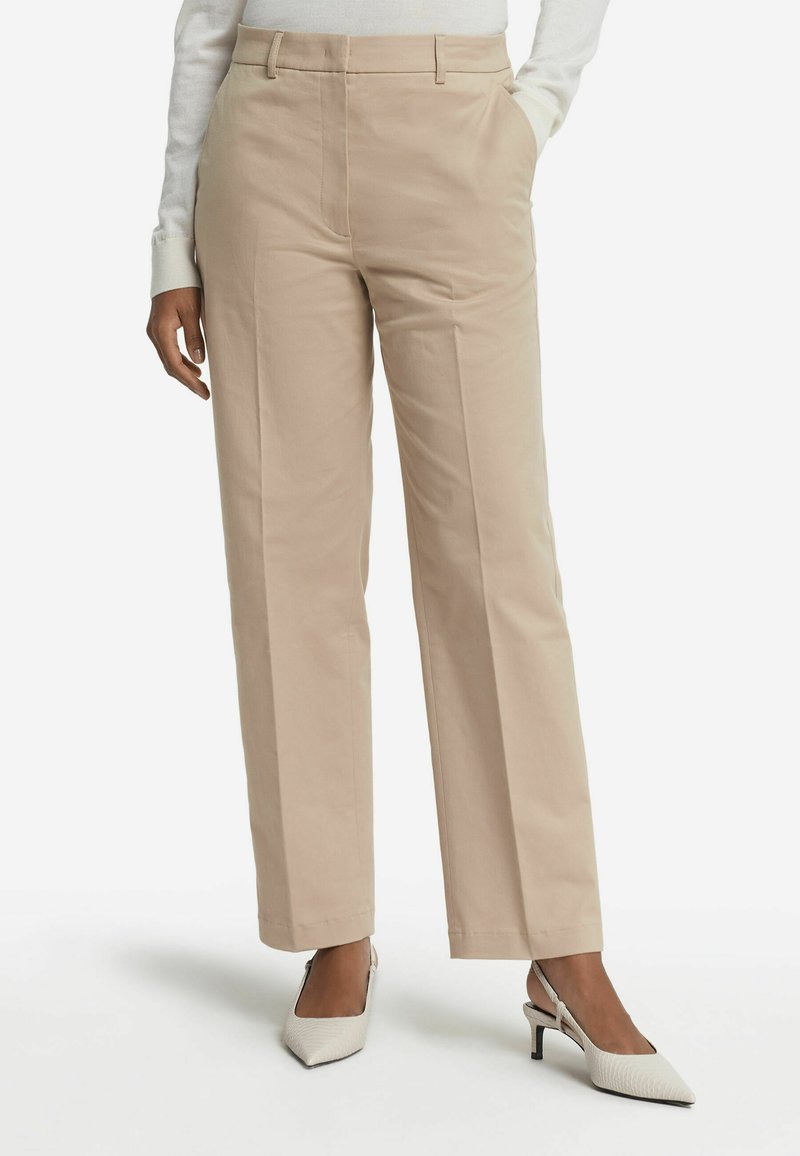 Beiga vida byxor i slät tyg, med en framveck och sidofickor. Bärs med vita klackar med slingback.