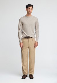 Hellgrauer langärmeliger Pullover, beige Chinos und braune Schuhe. Das Outfit zeichnet sich durch ein einfaches Design mit rundem Ausschnitt und glatter Textur aus.
