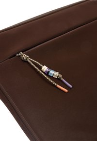 Zbliżenie brązowej torby na zamek błyskawiczny z multikolorowym uchwytem zamka oraz fioletowymi i pomarańczowymi końcówkami sznurków.