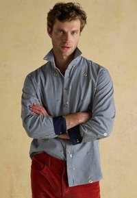 Prúžkovaná košeľa s button-up v modrej a bielej farbe s vyšitými detailmi; má tmavo-modrý golier a manžety, ľahký materiál, strih prispôsobený postave.