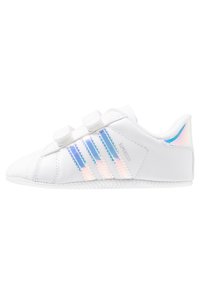 Vita småbarnssneakers med två kardborreband, iridescent blå-pink Adidas-ränder och texten "Superstar" på sidan.