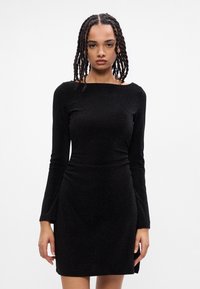 Abito nero a maniche lunghe con silhouette aderente, scollatura a barca e tessuto a shimmer testurizzato, con orlo leggermente svasato.