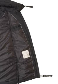 Intérieur d'une veste noire isolée avec une poche zippée et une étiquette. Présente une texture lisse, des coutures blanches contrastées et une étiquette de logo sur l'ourlet.