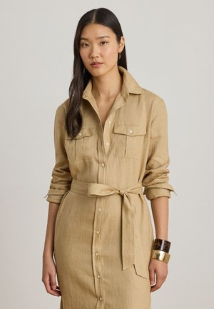 Noor naine, kes kannab beežika nuppudega kleiti rinnataskutega, üleskeeratud varrukatega, vööd seotud vööga ja kahe käepaelaga paremal randmel.